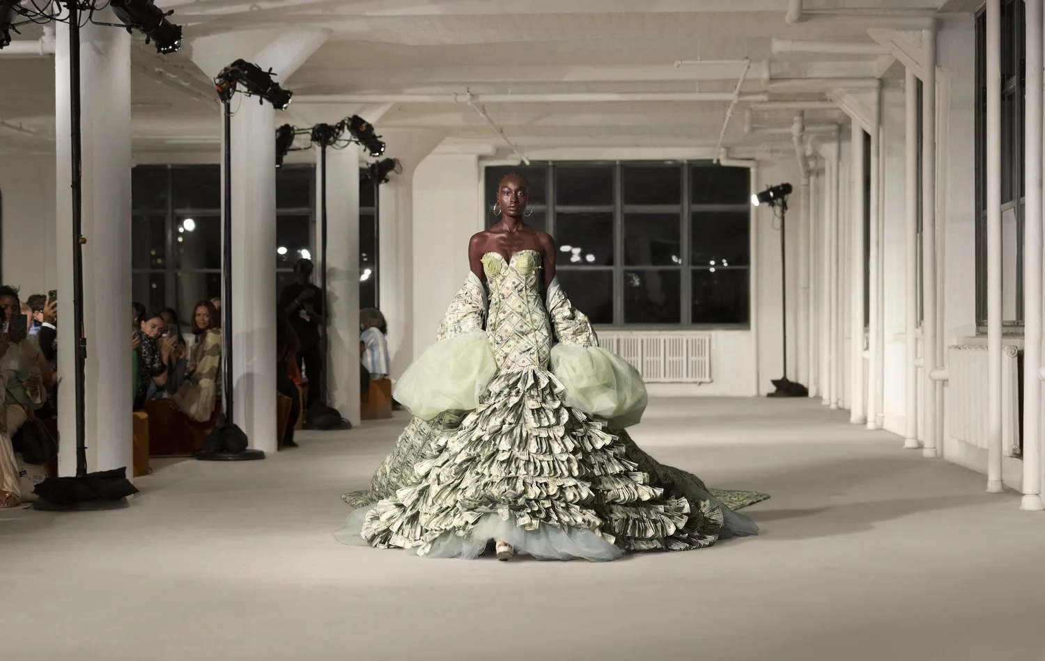 A model walks a runway wearing The Dre$$, a gown covered in currency-like fabric