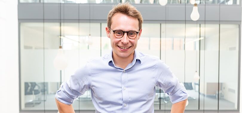 Martin Sweeney standing in a bright office, wearing glasses and a pale blue shirt