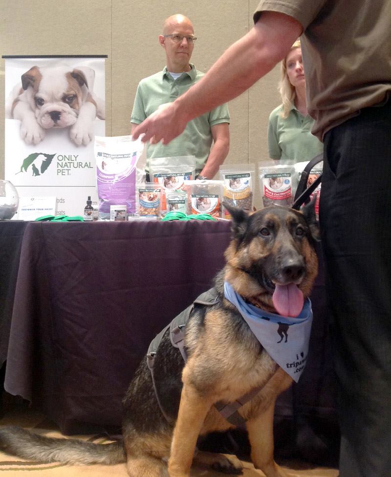 Marty Grosjean behind the Only Natural Pet booth at BlogPaws 2014, with German shepherd Wyatt in the foreground