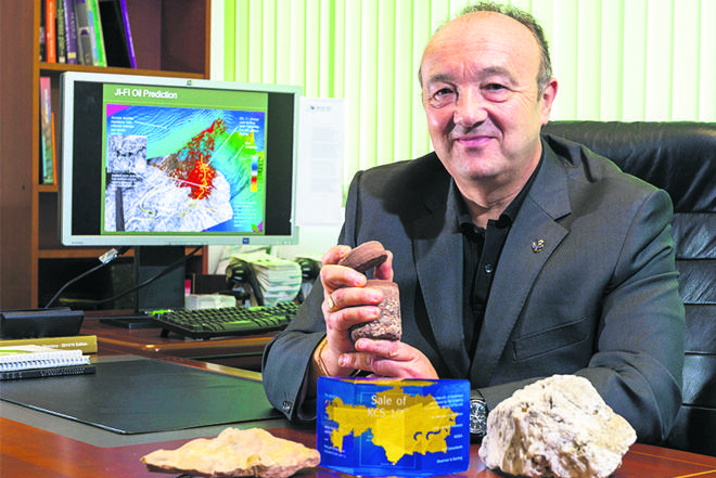 Martyn Millwood Hargrave holding a rock sample at his desk, with other specimens and a geoscience model on screen