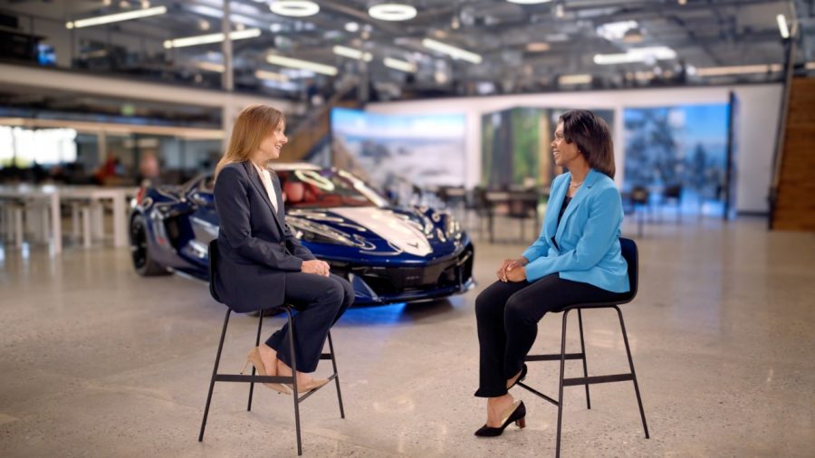 Mary Barra, left, and Condoleezza Rice seated in conversation with a blue sports car behind them.