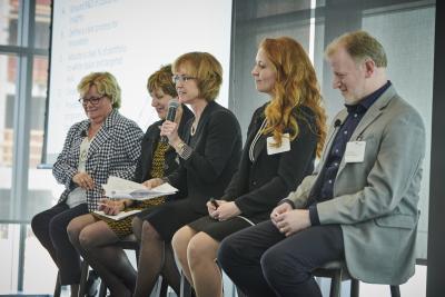 Mary Beth Moynihan speaks into a microphone while moderating a seated panel at the 2019 MedExecWomen conference