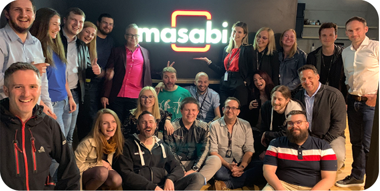 Masabi colleagues gathered for a team photograph in front of an illuminated company sign.