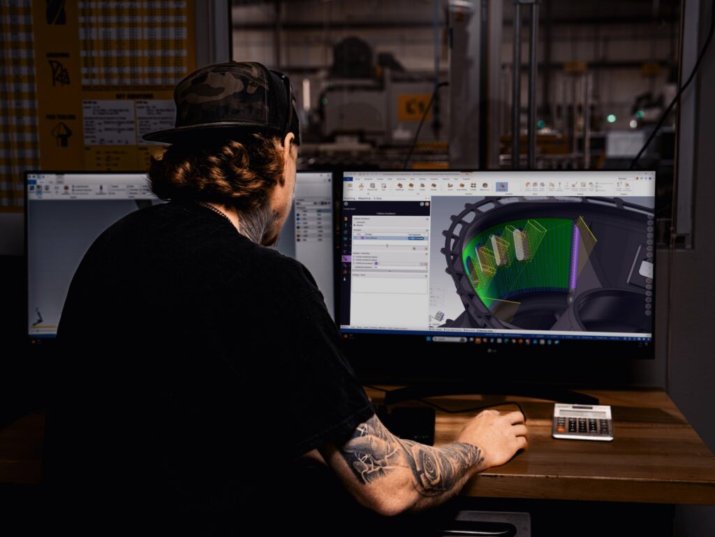 A programmer at a machine shop workstation reviewing complex toolpaths
