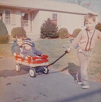 Archival childhood photograph of the three Summers brothers with a wagon