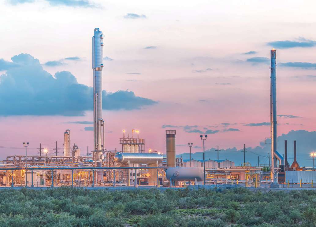 Black River natural gas processing plant in New Mexico, its towers and pipework illuminated beneath a pink evening sky