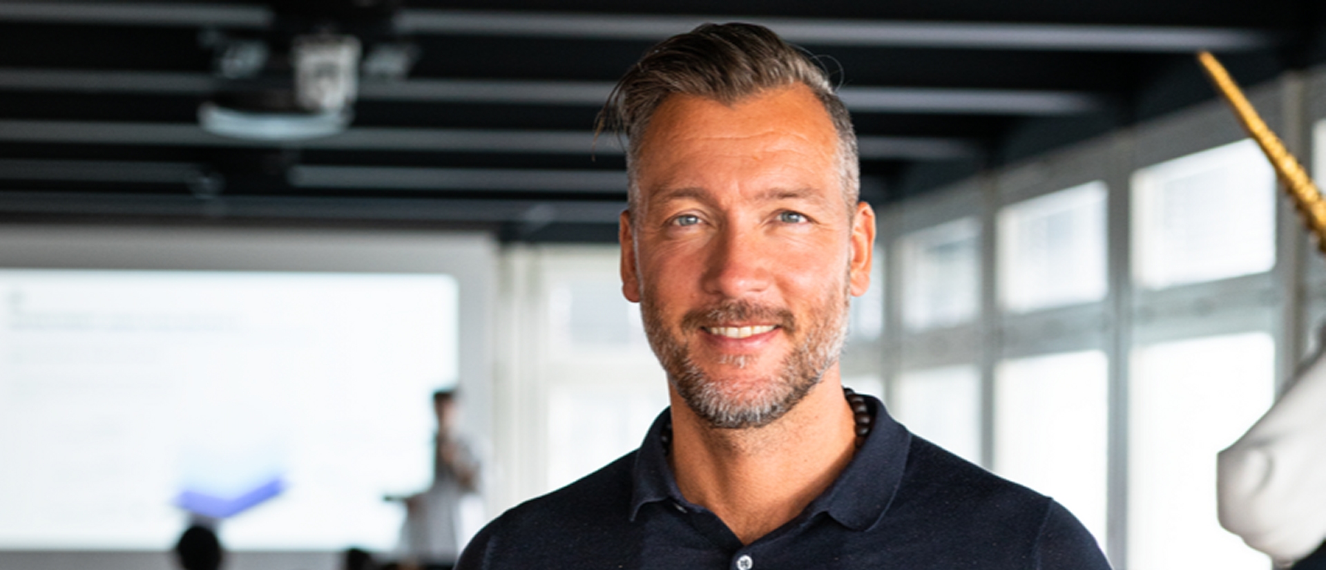 Mathias Ruch photographed indoors in a dark polo shirt, with a bright workspace behind him
