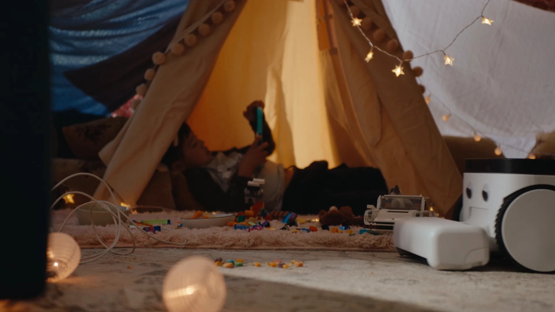 The Matic robot vacuum parked on the floor beside a child's indoor blanket fort at night