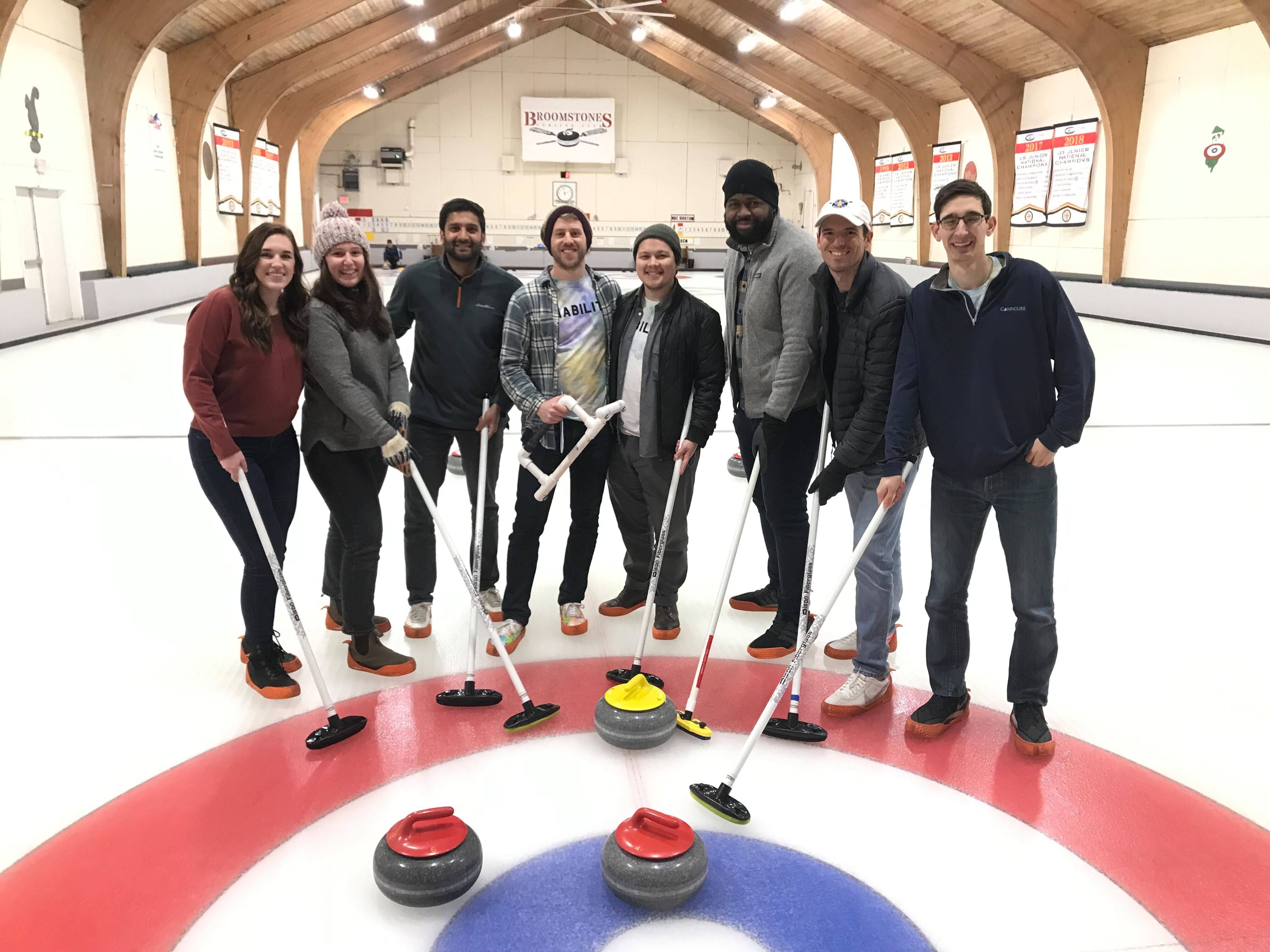 Herald colleagues holding curling brooms on the ice at Broomstones curling club