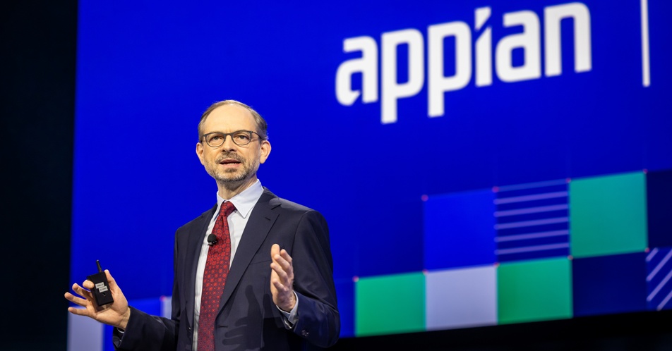 Matthew Calkins speaking on the blue-lit Appian World stage in 2023