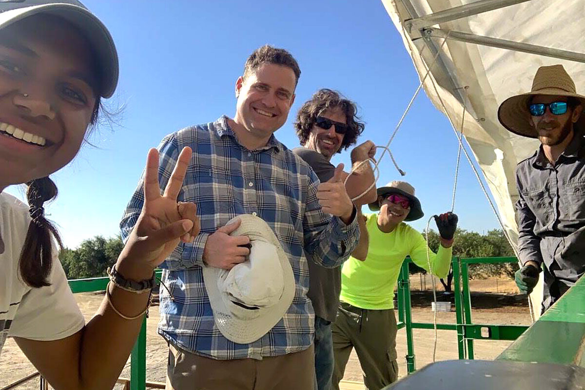 Matt Campbell in a plaid shirt, smiling with colleagues beside field equipment