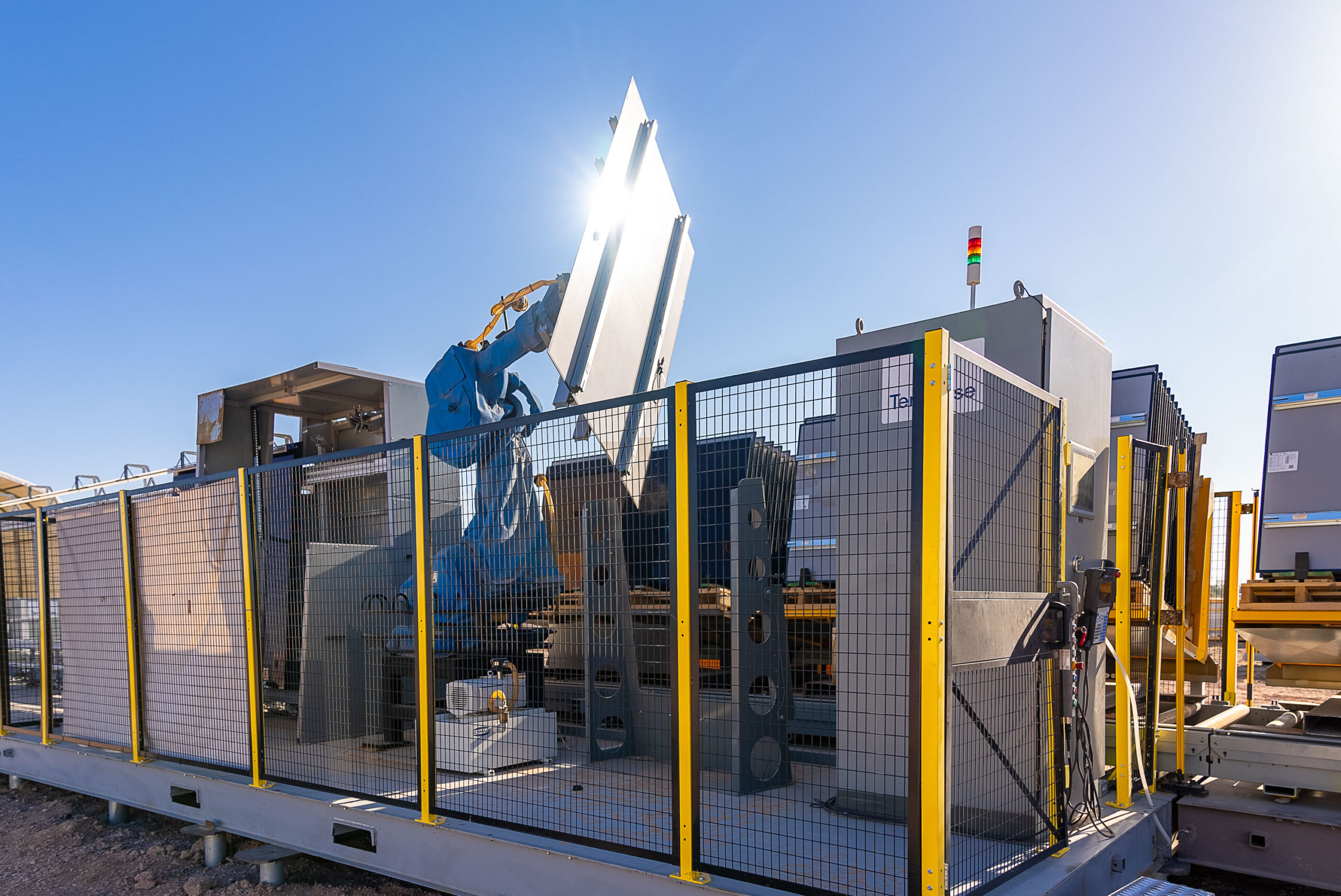 A robotic arm handling solar modules inside Terafab assembly equipment outdoors