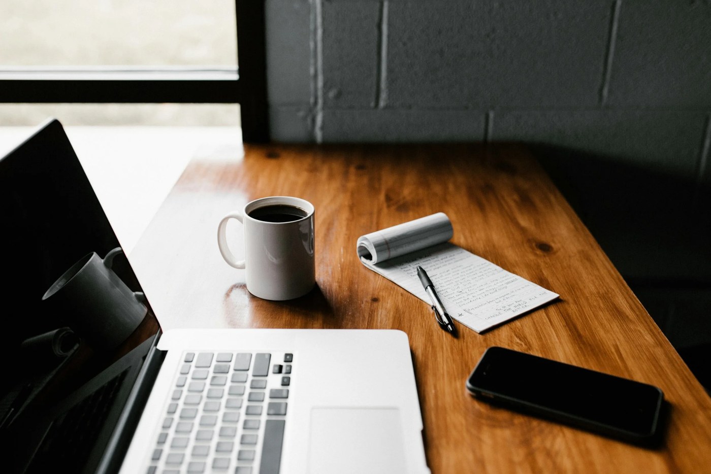 A writing table with coffee, a notepad, laptop, and phone