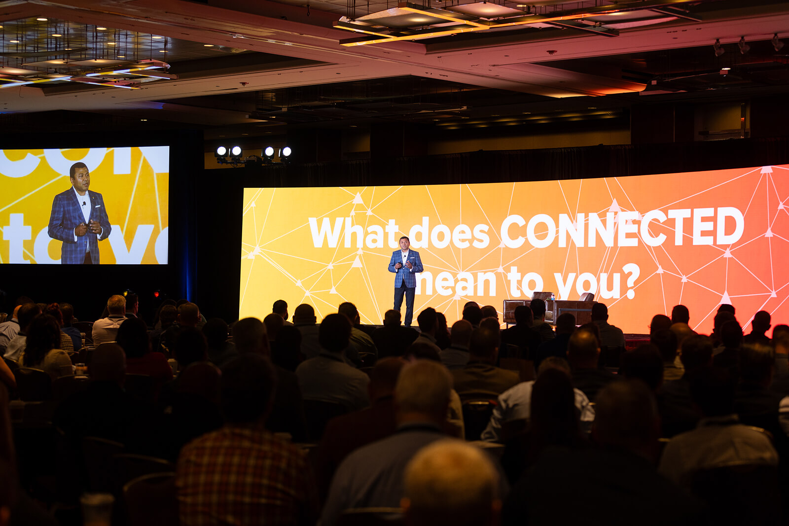 Mathew Elenjickal speaking on a conference stage before a screen asking what connected means to the audience