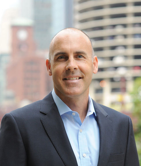 Historical press photograph of Matt Knott in a jacket, with buildings behind him