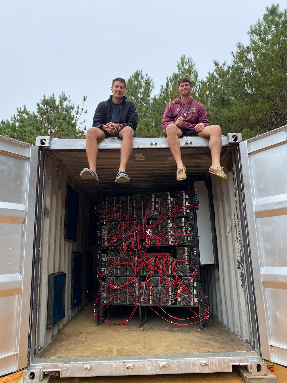 Matt Lohstroh, left, and Brent Whitehead sitting above the open doors of a container holding bitcoin mining equipment