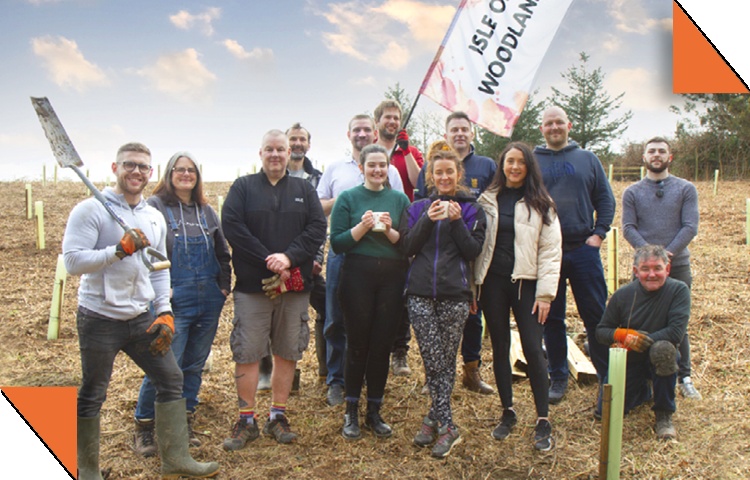 Matt Newing with a group outdoors among planted saplings, with spades and gardening gloves.