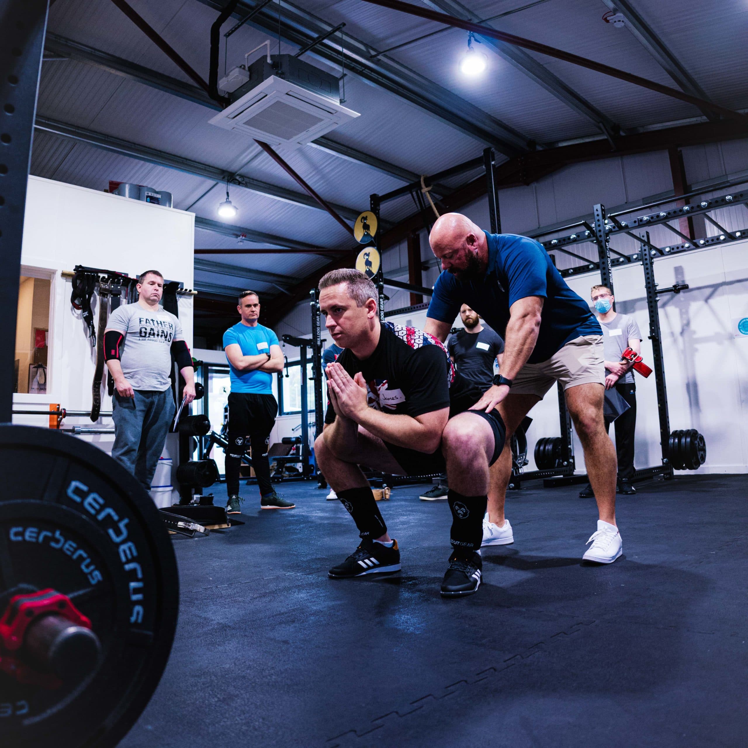 Matt Reynolds in a blue shirt coaching a squat while a small group watches