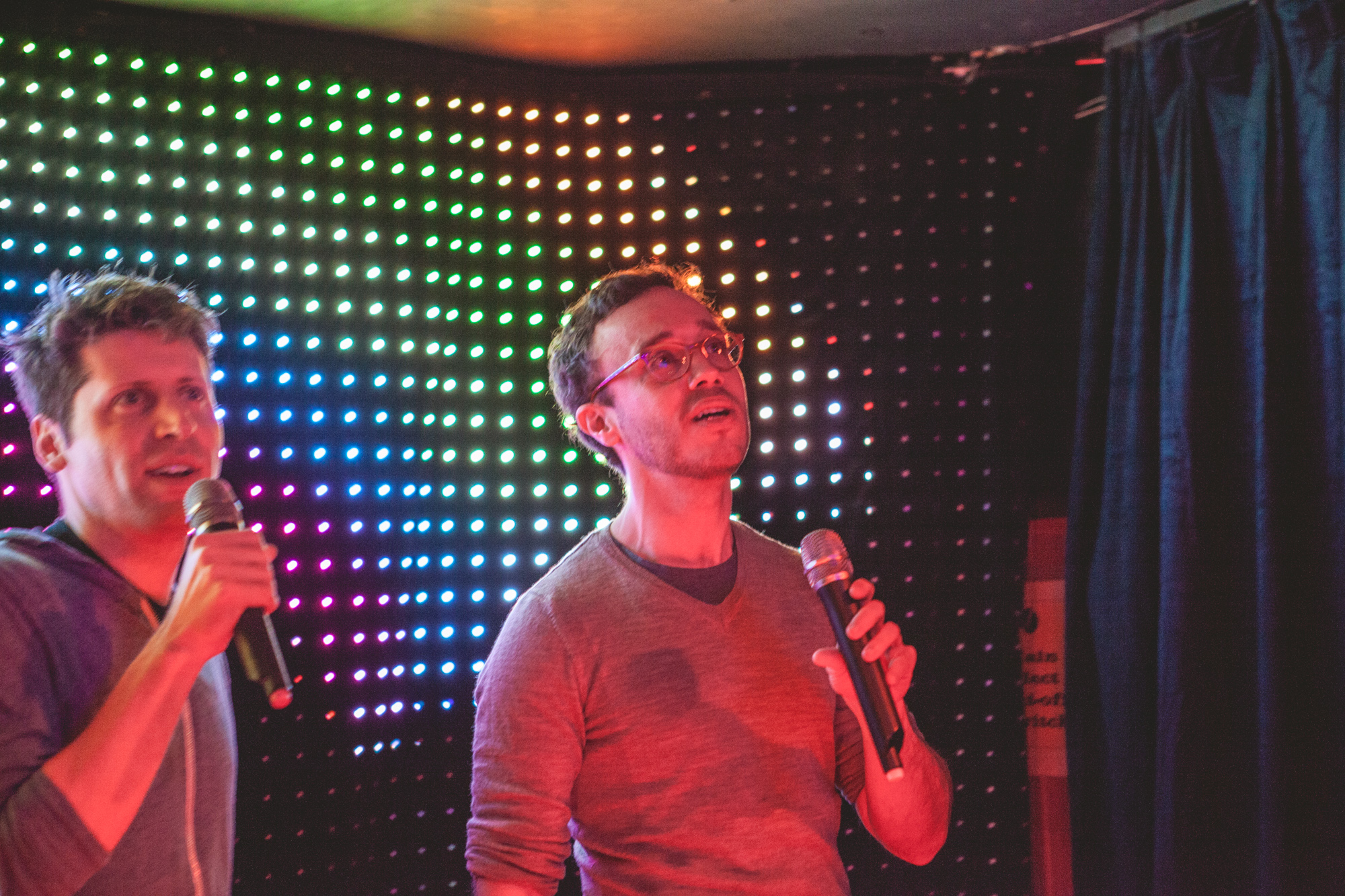 Sam Altman, left, and Matt Schiller, right, singing karaoke under coloured lights