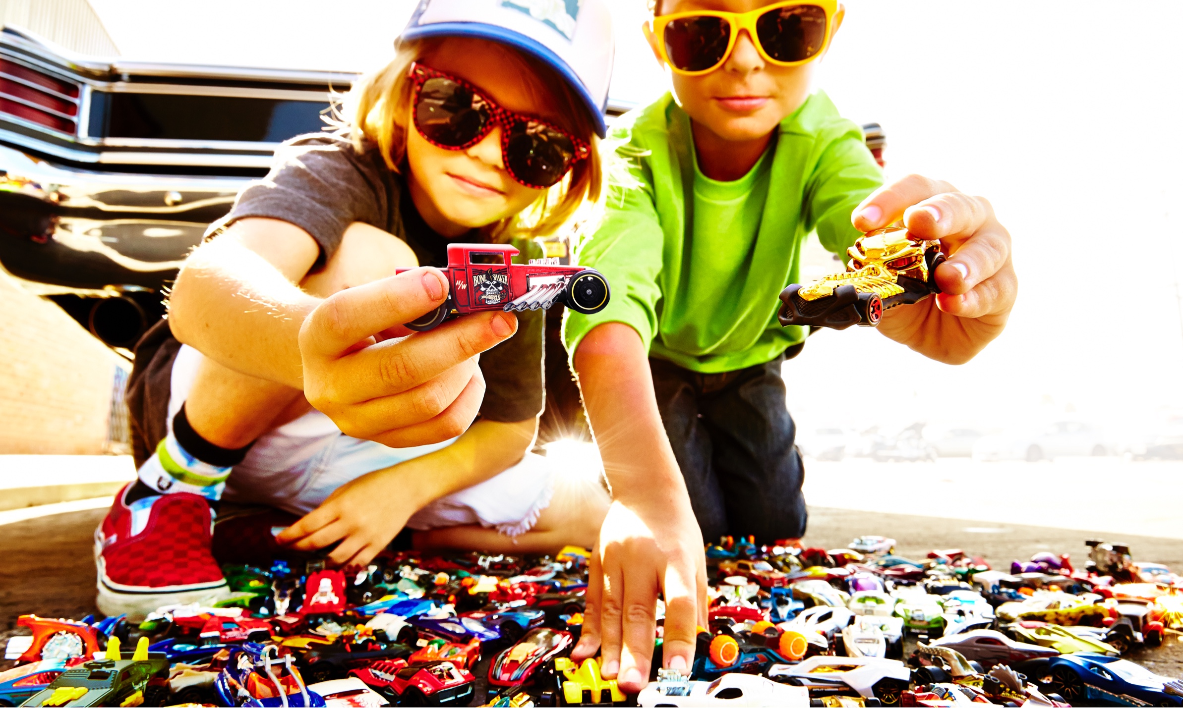 Two children holding Hot Wheels vehicles above a collection of toy cars