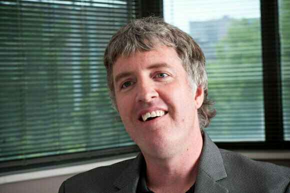 Matthew Dornquast smiling, seated beside an office window