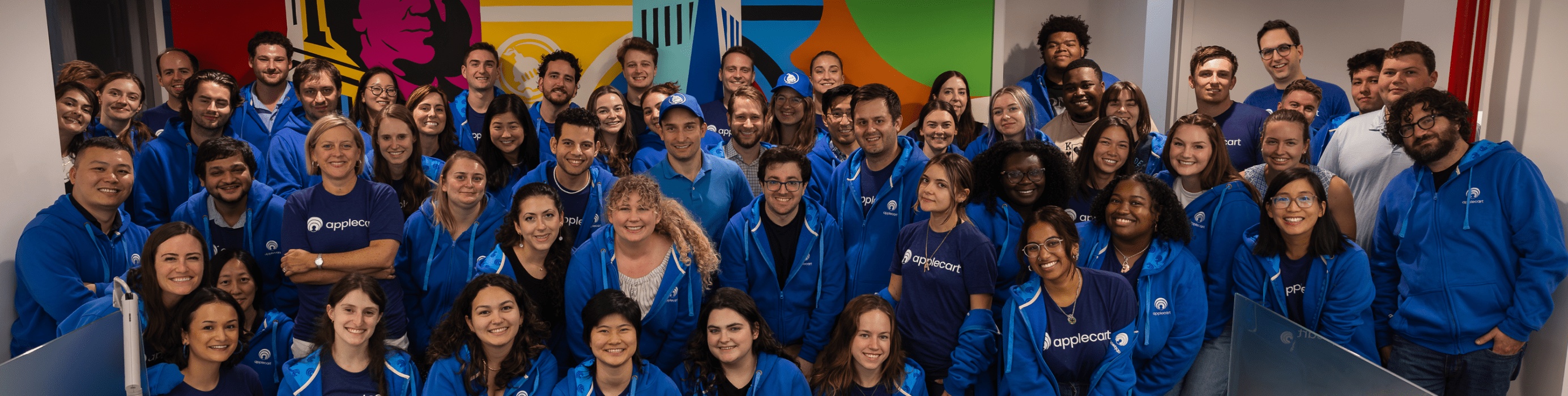Applecart colleagues gathered in their office wearing blue company sweatshirts