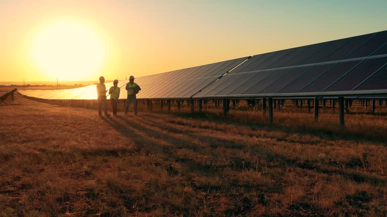 Solar-energy specialists walking between rows of panels at sunset