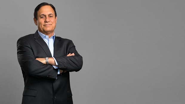 Matthew Rizai in a dark suit with his arms folded, against a gray background