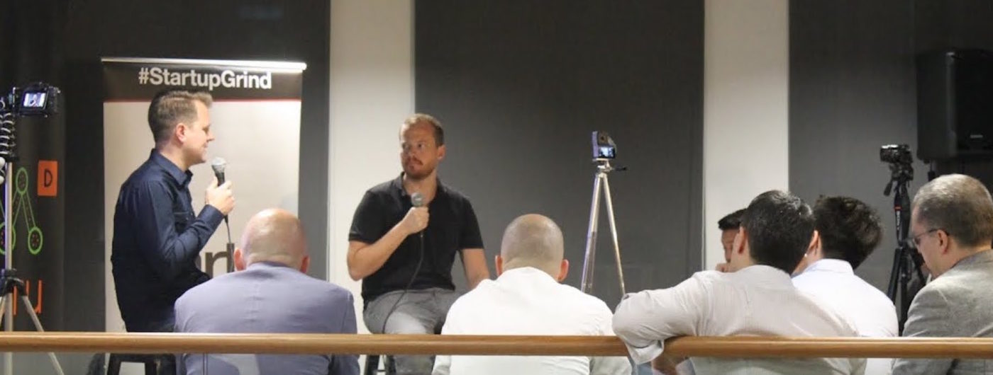 Matthew Tillman, on the left, speaking into a microphone during a Startup Grind discussion