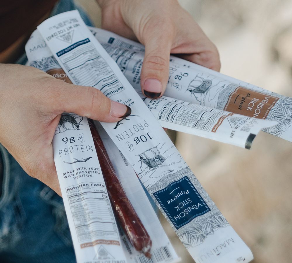 Hands holding an assortment of Maui Nui Venison snack sticks
