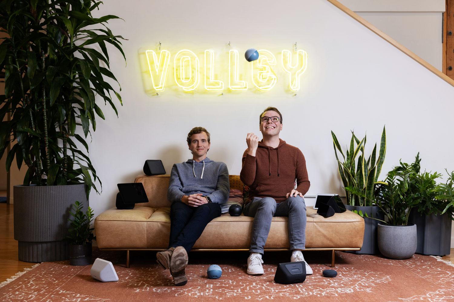 Max Child, left, and James Wilsterman seated on a sofa beneath the Volley sign, surrounded by smart speakers.
