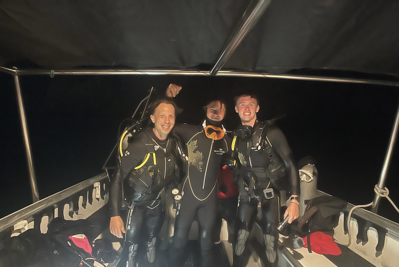 Max Gallinek, right, on a boat in scuba gear with two other divers at night