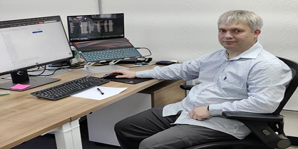 Max Mikheev seated at a workstation with a monitor and laptop