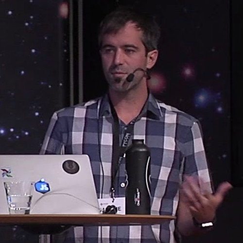 Maxime Beauchemin speaking at a podium with a sticker-covered laptop