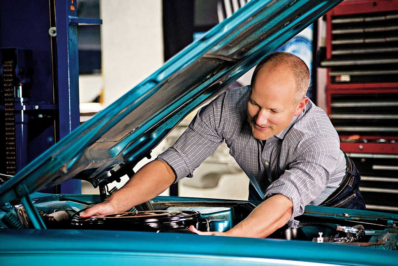 McKeel Hagerty leaning into the engine bay of a blue car in a workshop