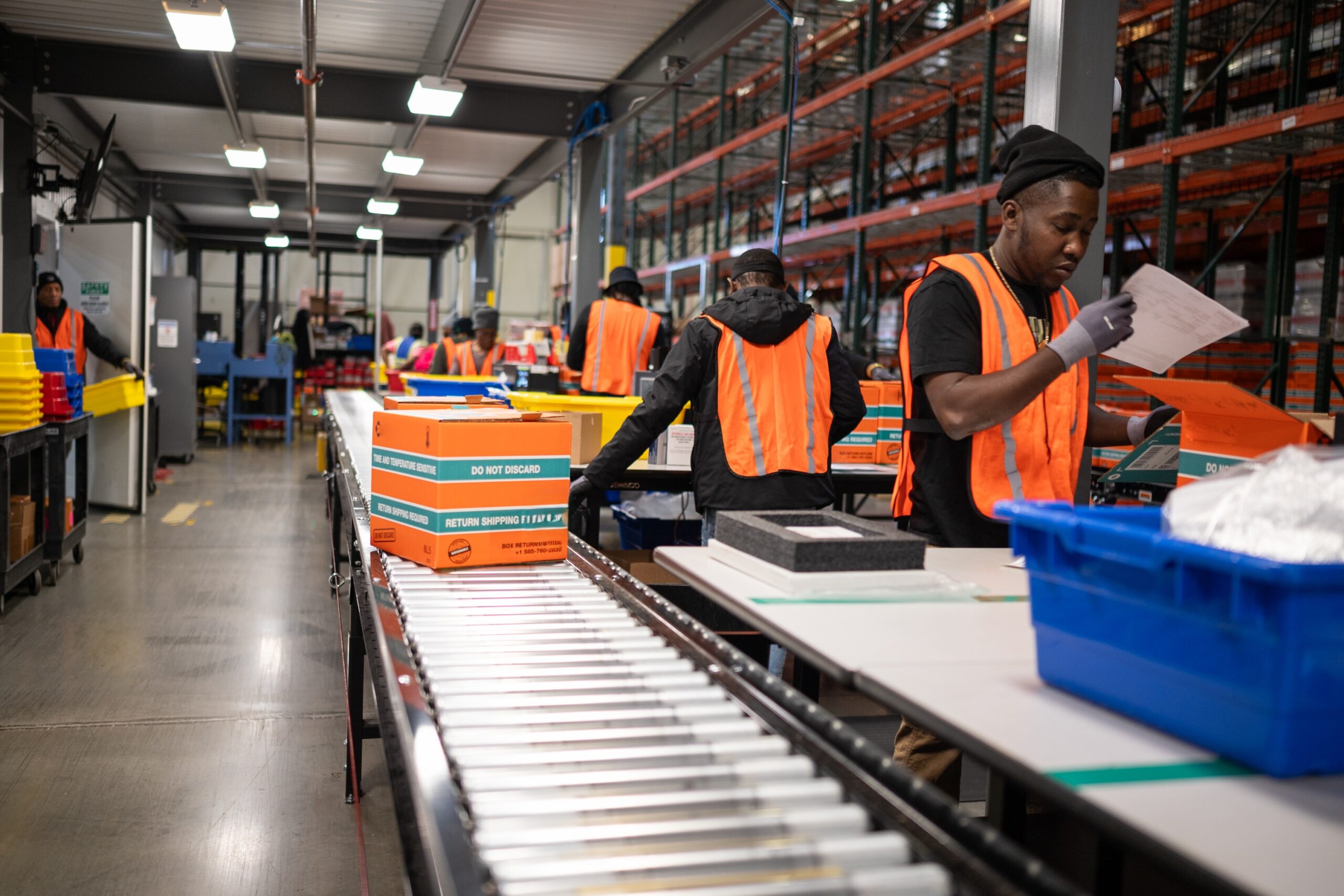 Warehouse associates preparing orange reusable AeroSafe shipping boxes on a conveyor