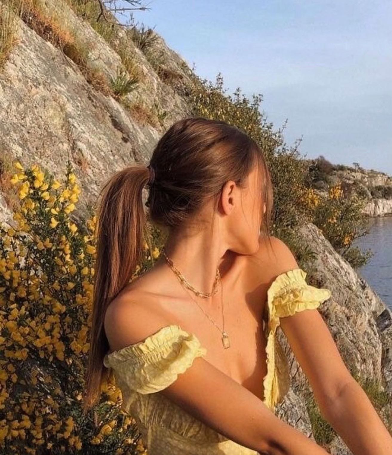 Madeline Elizabeth’s public Medium portrait, seated beside a rocky shoreline in a yellow outfit