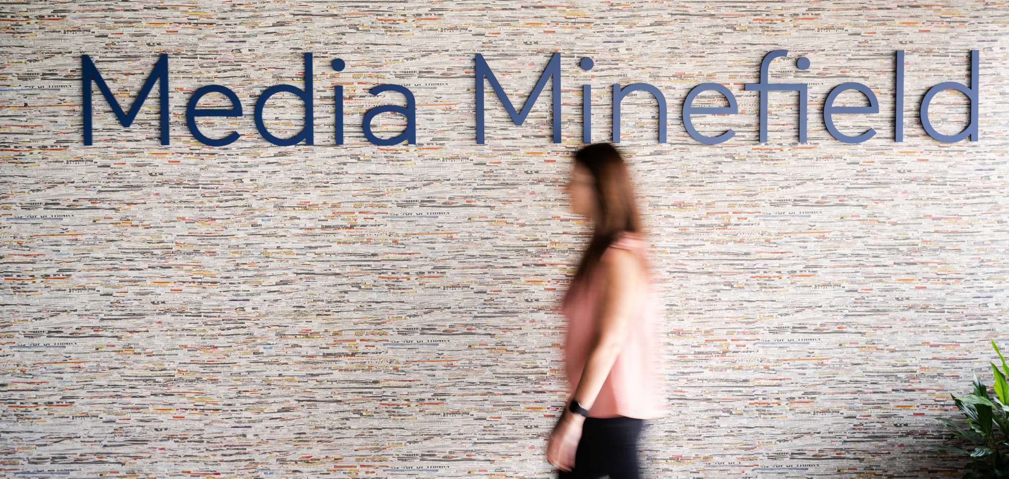 A person walking past the Media Minefield name mounted on a wall made of strips of newsprint