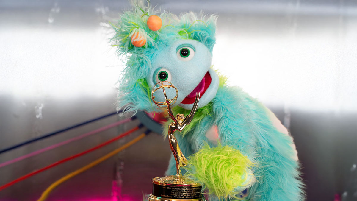 Alax, the turquoise three-eyed character from The Early Show with Alax, holding a regional Emmy award