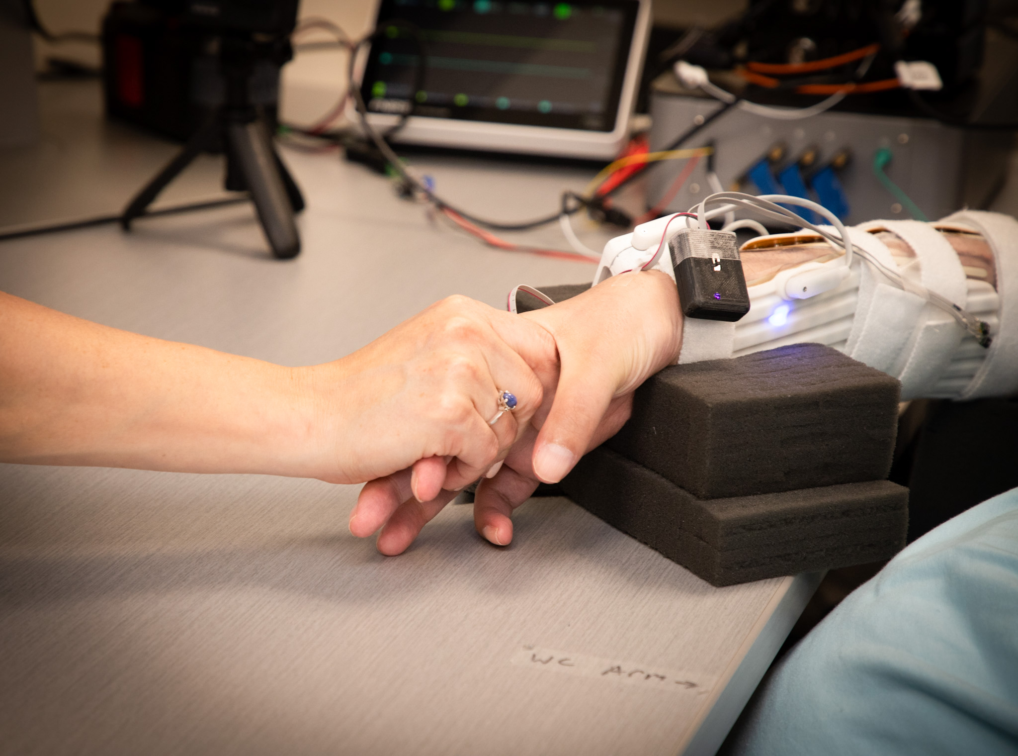 A patient wearing sensors on his forearm holds his sister's hand during a neural bypass trial