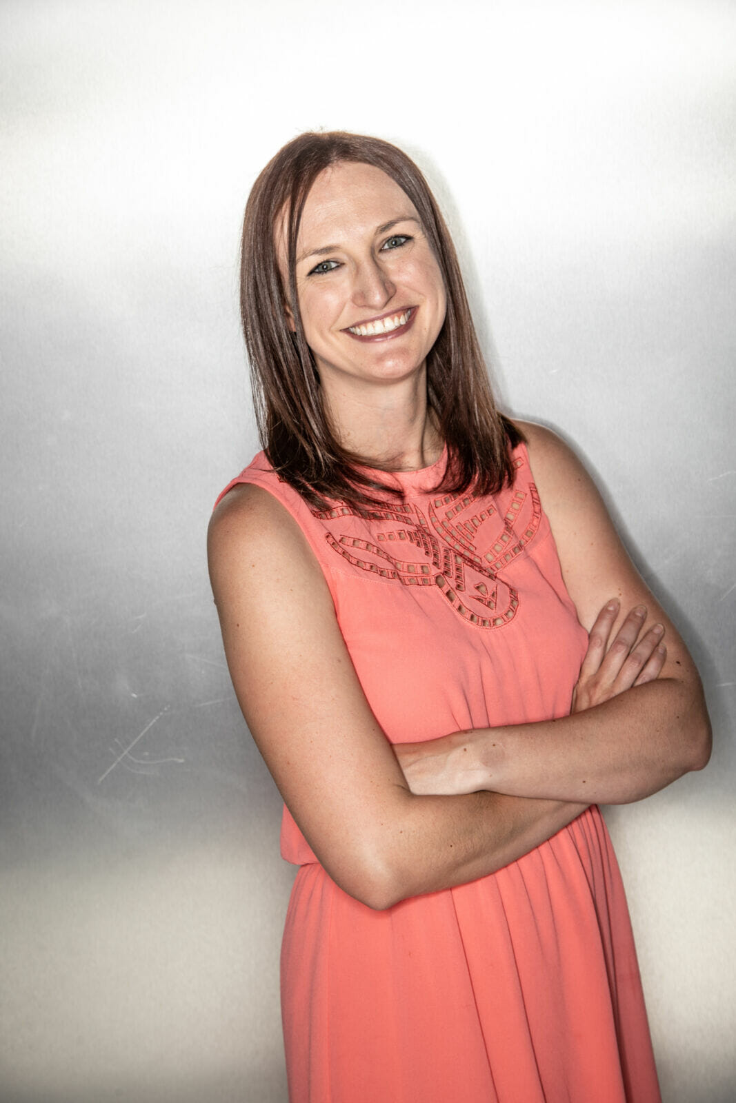 Megan Simoes in a coral dress, smiling with her arms folded