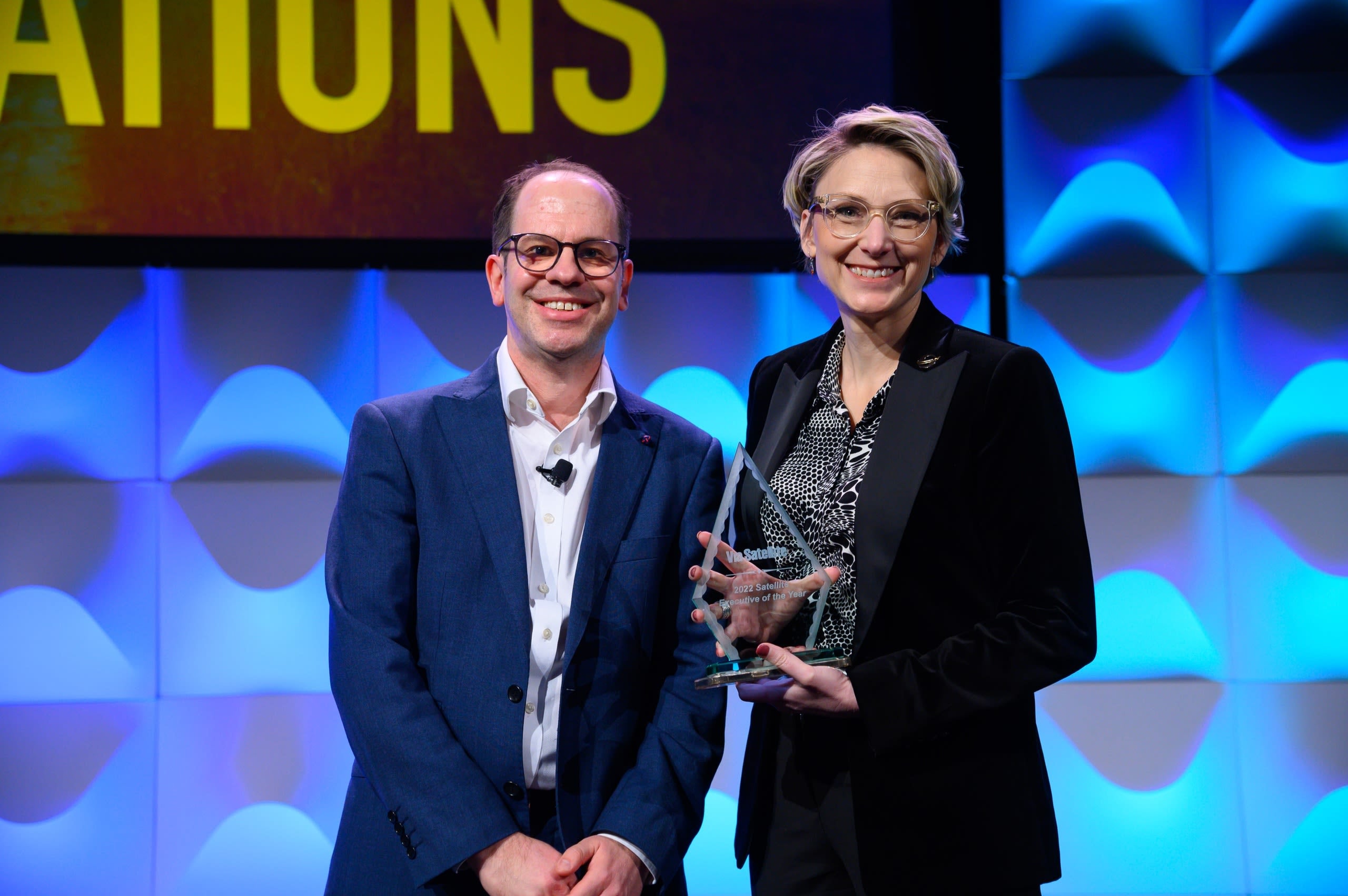 Melanie Stricklan, right, holding her Satellite Executive of the Year award onstage.