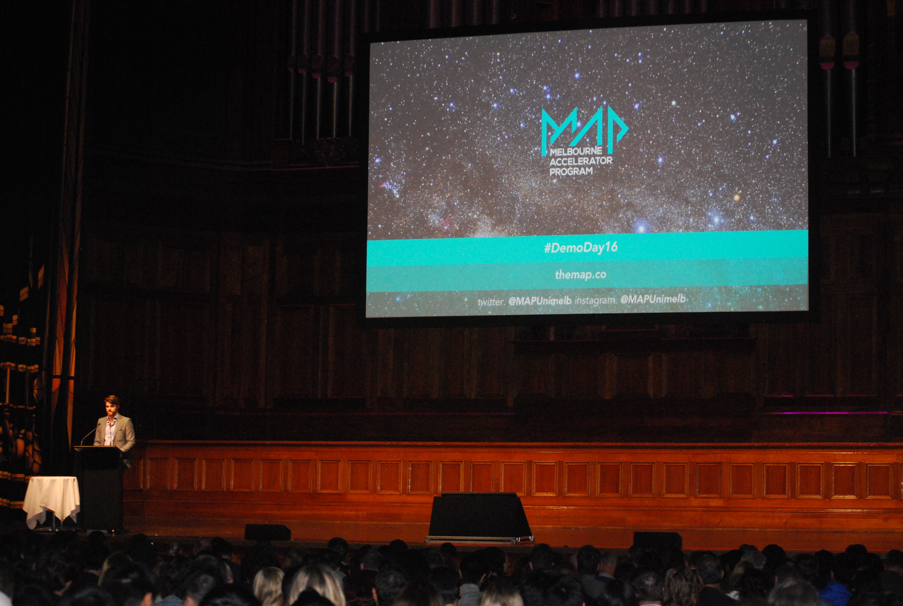 A speaker addresses the audience beneath a MAP Demo Day 2016 projection