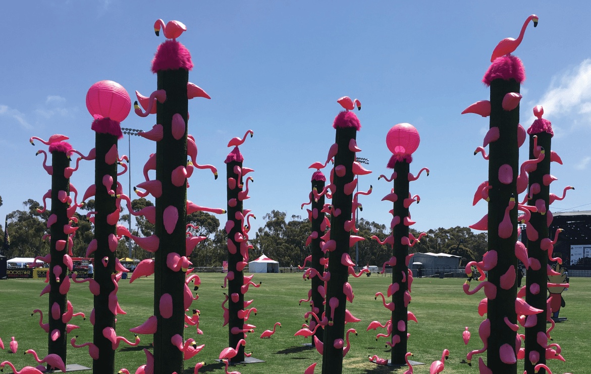 Pink lawn flamingos attached to tall green columns at Sun God Festival