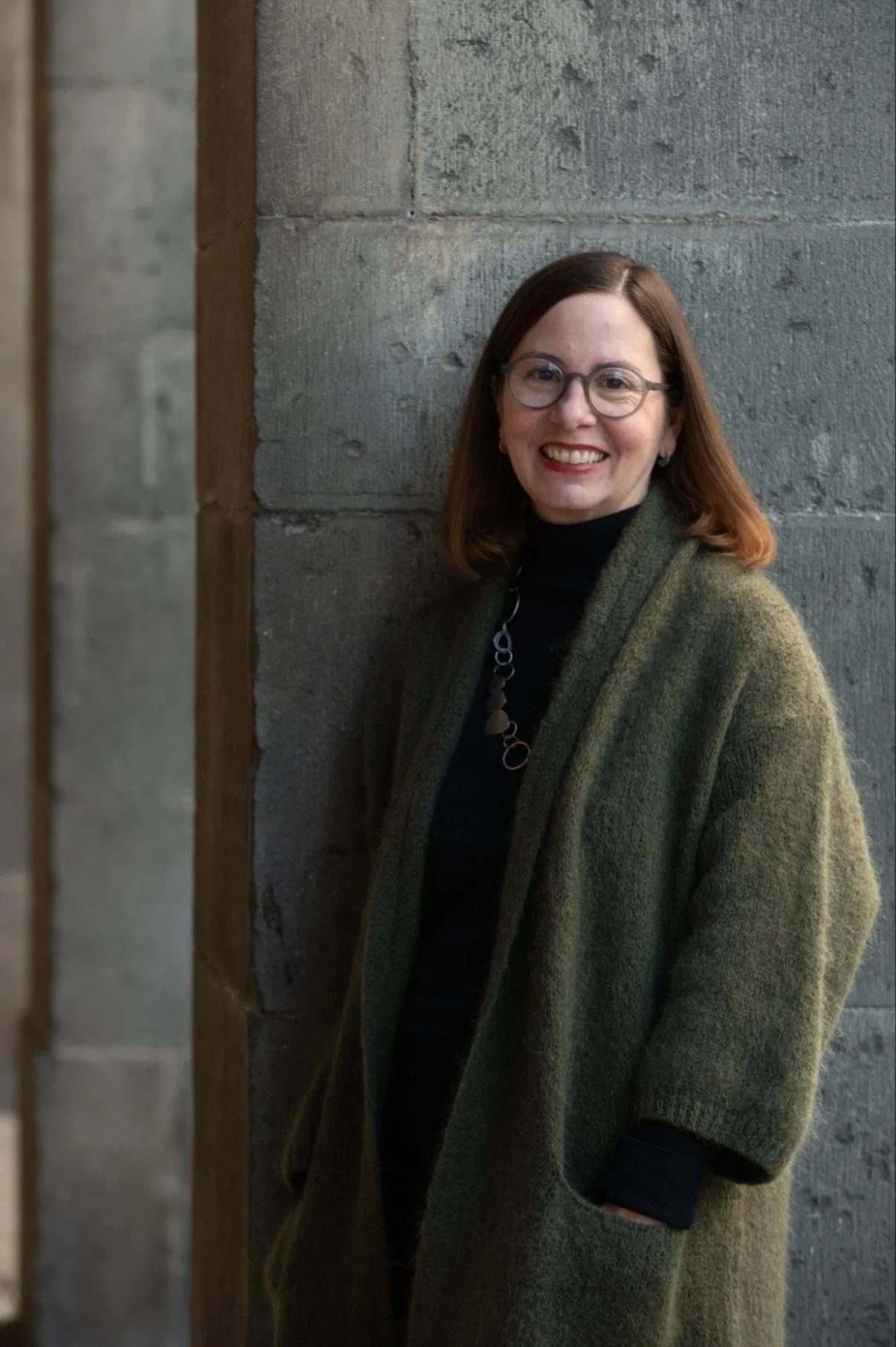 Melissa Marshall wearing glasses and a green cardigan beside a stone wall