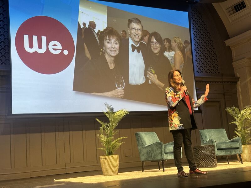 Melissa Waggener Zorkin speaking onstage at the Microsoft 50th anniversary event, with an early photograph projected behind her