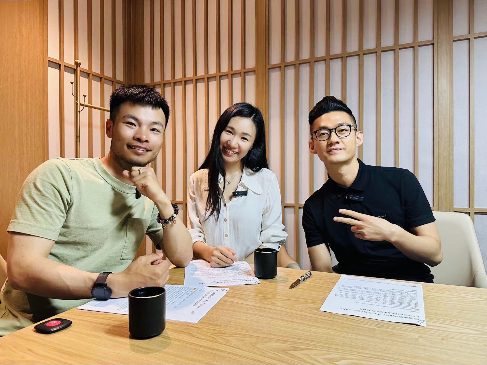 MK Li, left, seated at a restaurant table with the hosts of 出海相对论, with notes and cups on the table