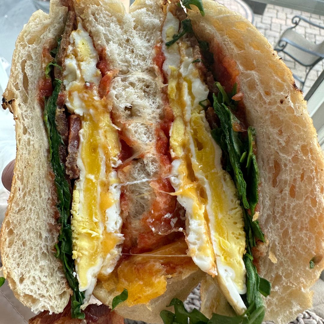 Cut breakfast sandwich showing egg, bacon, greens and tomato inside bread