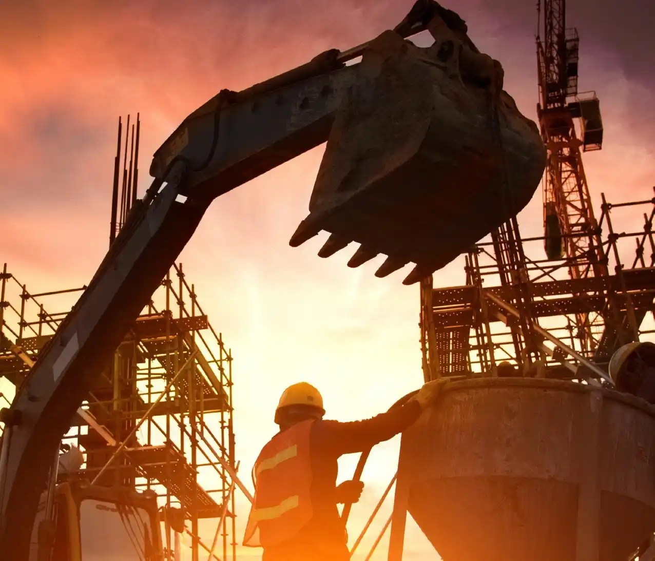 Construction machinery and a worker silhouetted against a warm evening sky