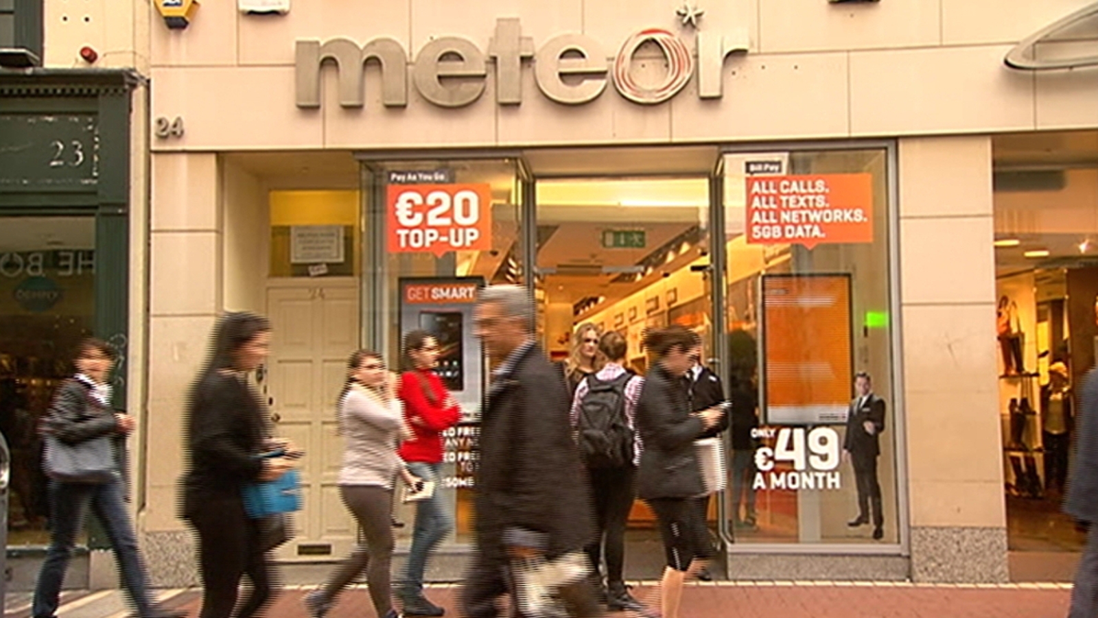 A Meteor shop with orange tariff posters and pedestrians passing outside